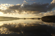 Golden morning light is illuminating clouds towering over a glassy forest lake by Intensivelight Panorama-Edition