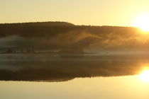 Wisps of haze are rising from a forest at the shore of a glassy lake at sunset by Intensivelight Panorama-Edition