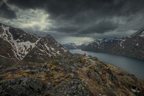 Woman hiking along blue lake in mountain landscape on hike of Knutshoe in Jotunheimen National Park in Norway by Bastian Linder