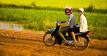 Mädchen reiten auf einem Feldweg in Kambodscha. von Jason Friend