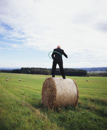 Rear view of a man standing on a hay bale playing with a plastic hoop, Germany von Panoramic Images