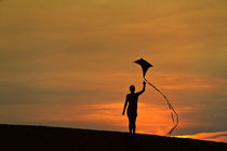 Silhouette of a child flying a kite. by John Greim