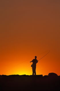 Boy fishing from a jetty. by John Greim