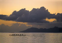 An outrigger canoe team practices off the coast of the island of Tahiti as the sun sets over the island of Moorea in the Society Islands of French Polynesia von Danita Delimont