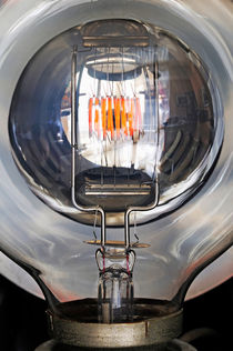 Red filament inside illuminated light bulb by Sami Sarkis Photography