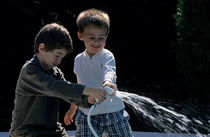 Two boys (11-13) playing with garden hose by Sami Sarkis Photography