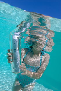 Girl (6-7) in pool holding bottle with SOS message von Sami Sarkis Photography