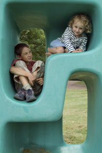 Boy (11-13) and girl (5-7) playing in plastic cube by Sami Sarkis Photography