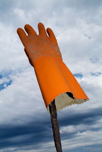 Orange rubber glove on a wooden post against a cloudy sky by Sami Sarkis Photography
