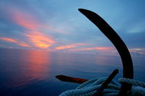 Rusty anchor with rope coiled around and view of the sunset over the sea in the background von Sami Sarkis Photography