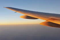 Wings of flying airplane over  clouds at sunset by Sami Sarkis Photography