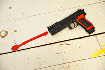 Toy gun on floor with red paint by Sami Sarkis Photography