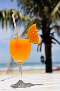 Glass of Orange cocktail by palm tree on beach by Sami Sarkis Photography