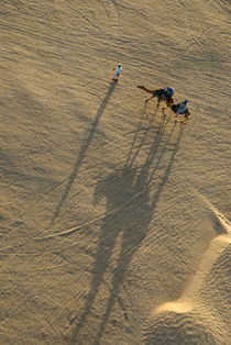 Man leading two camels with tourists at sunset by Sami Sarkis Photography