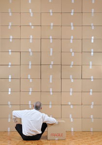 Businessman seated facing cardboard boxes wall by Sami Sarkis Photography