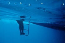 Bare legs descending underwater from the ladder of a boat by Sami Sarkis Photography