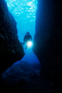 One scuba diver shines an underwater light while swimming through a cave von Sami Sarkis Photography