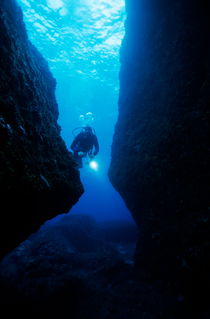 One scuba diver shines an underwater light while swimming through a cave by Sami Sarkis Photography