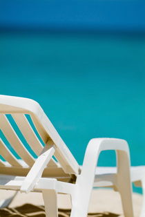 Empty white deck chair on a beach with bright blue waters by Sami Sarkis Photography