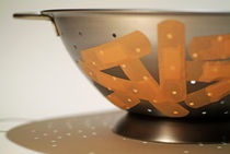 Metallic colander covered with sticking plasters. by Sami Sarkis Photography