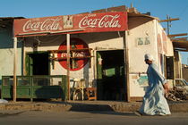 Man dressed in traditional Islamic dress walks by a coffee shop by Sami Sarkis Photography