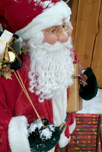 Santa Claus toy standing next to Christmas presents in the snow. by Sami Sarkis Photography