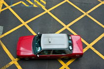 Red taxi cab driving over yellow lines von Sami Sarkis Photography